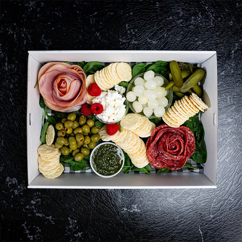 An Antipasto platter with an assortment of deli meats, cheese, crackers, and pickles arranged in a box.