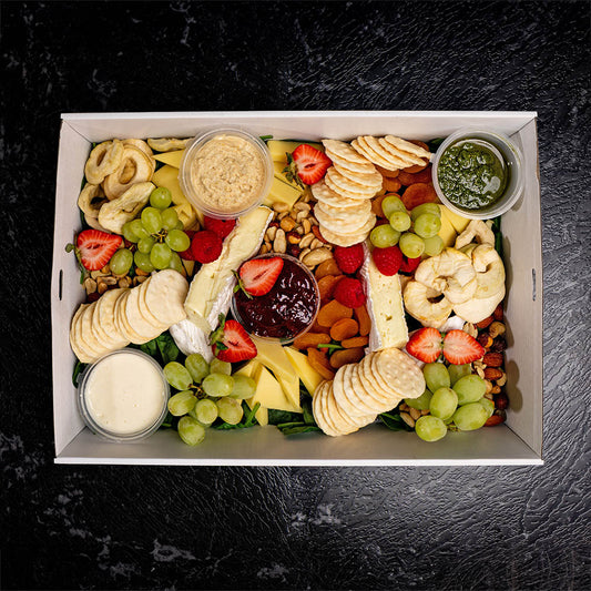 A Grazing platter with an assortment of fresh and dried fruits, crackers, cheeses, dips, and nuts arranged in a box.